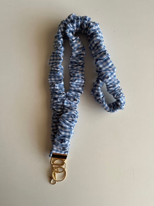 Blue and white checkered lanyard with a gold clip on a beige background